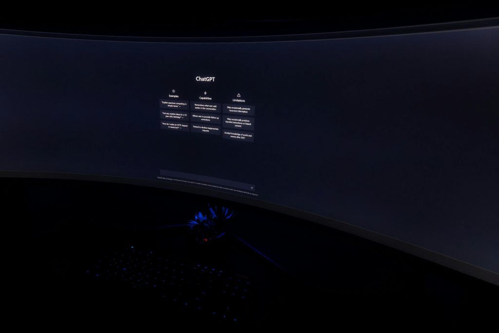 Close-up of a dark room with a curved monitor showing the ChatGPT interface on screen.